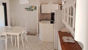 A modern kitchen with white cabinets, a wooden countertop, and a dining area with a white table and chairs. - Eden Rock sea View  (Eden Rock)
