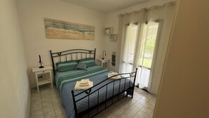 A bedroom with a bed, nightstands, a painting, and a window with curtains. - Eden Rock sea View  (Eden Rock)