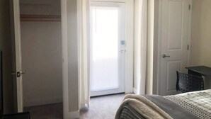 Een slaapkamer met een bed, een kast, een deur en een klein tafeltje.