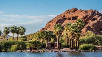 A serene lakeside setting with a stone structure, palm trees, and a large rock formation in the background.