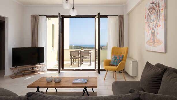 A modern living room with a flat-screen TV, a wooden coffee table, a sofa, a yellow armchair, and a balcony with a view. - Mela Villa Lemon with Private Pool, Eco Friendly (ΡΕΘΥΜΝΟ)