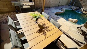 A wooden table with chairs, a grill, and a small pool with rocks and a waterfall feature. - Casa Del Sol Gilbert, Arizona Heated Pool & Hot Tub (Gilbert)