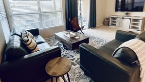 A living room with a sofa, a coffee table, a TV, and a ceiling fan. - Casa Del Sol Gilbert, Arizona Heated Pool & Hot Tub (Gilbert)
