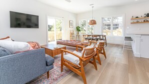 A spacious living room with a grey sofa, wooden dining chairs, a coffee table, and a TV mounted on the wall. - Luxury heated pool & spa home, pool bar, steps to the beach & two master suites! (St. Augustine)
