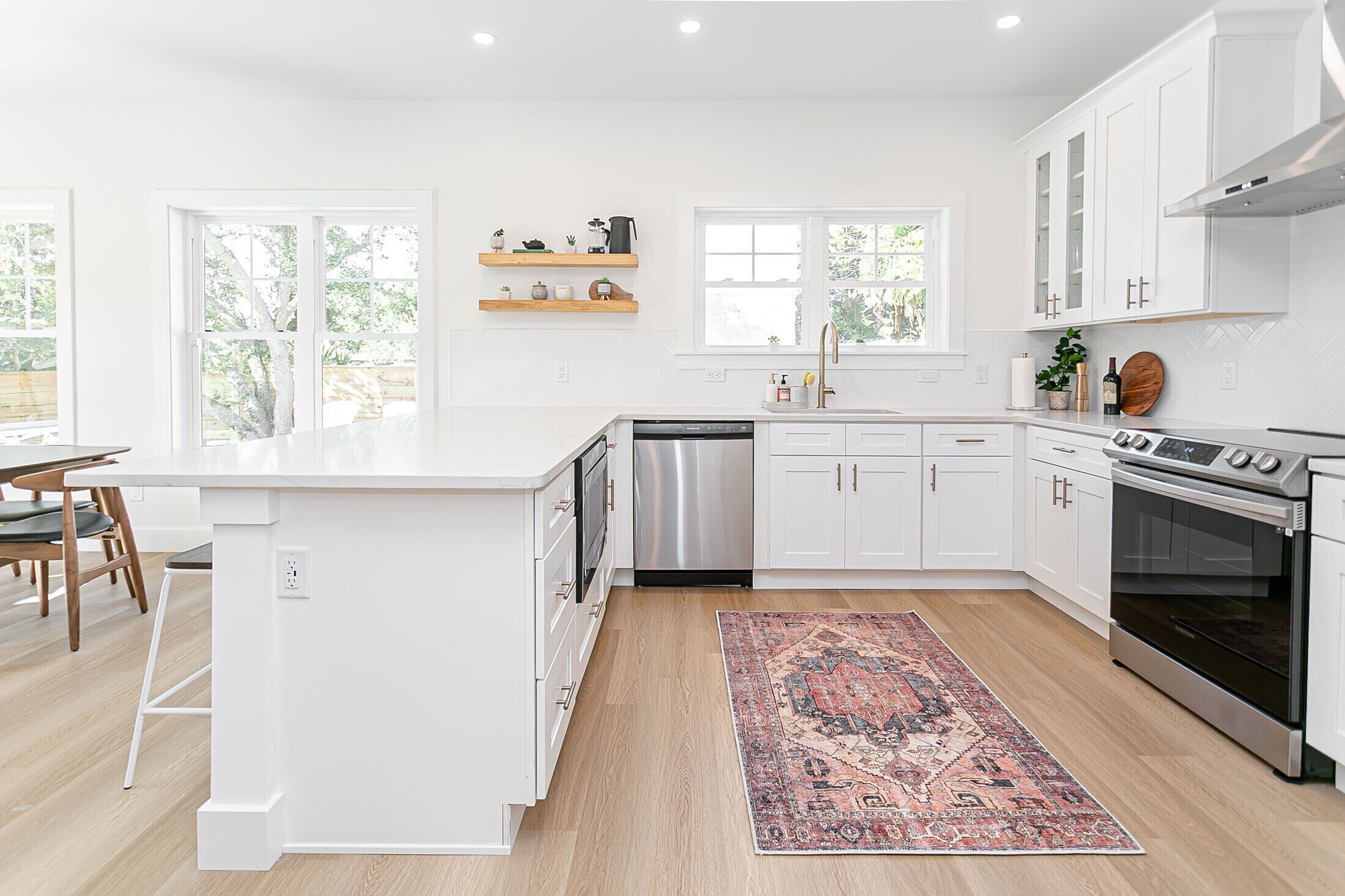 A modern kitchen with white cabinetry, a dishwasher, an oven, and a window providing natural light.