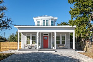 Ein modernes Haus mit roter Tür, zwei überdachten Veranden und einem kleinen Vorgarten.
