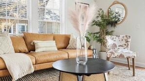 A living room with a brown leather sofa, a round black table, a chair with a spotted pattern, a large potted plant, and a round mirror on the wall. - ✰ MARSH VIEW - CHARMING 3BR/2.5BA - BIKES/KAYAKS ✰ (North Charleston)