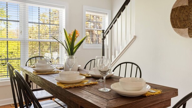 A dining table set with plates, glasses, and a vase with flowers, with a staircase and windows in the background. - ✰ MARSH VIEW - CHARMING 3BR/2.5BA - BIKES/KAYAKS ✰ (North Charleston)
