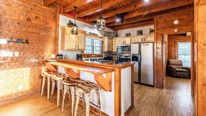 A wooden cabin interior with a kitchen area featuring a bar and stools, a refrigerator, and wooden ceiling beams. - Pet friendly,5min2Dollywood,3 kings+loft,Game Room (Pigeon Forge)