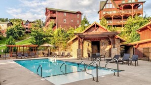 A pool area with lounge chairs and a covered seating area, surrounded by buildings with a rustic architectural style. - Pet friendly,5min2Dollywood,3 kings+loft,Game Room (Pigeon Forge)