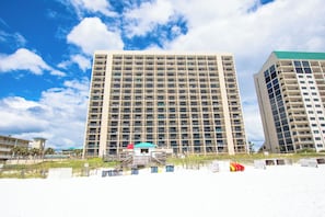 Un immeuble de grande hauteur doté de nombreux balcons, une plage au premier plan et un ciel dégagé.
