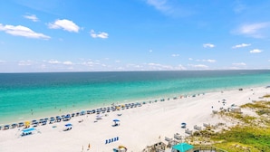 A beach with white sand, clear turquoise water, and a line of blue umbrellas.