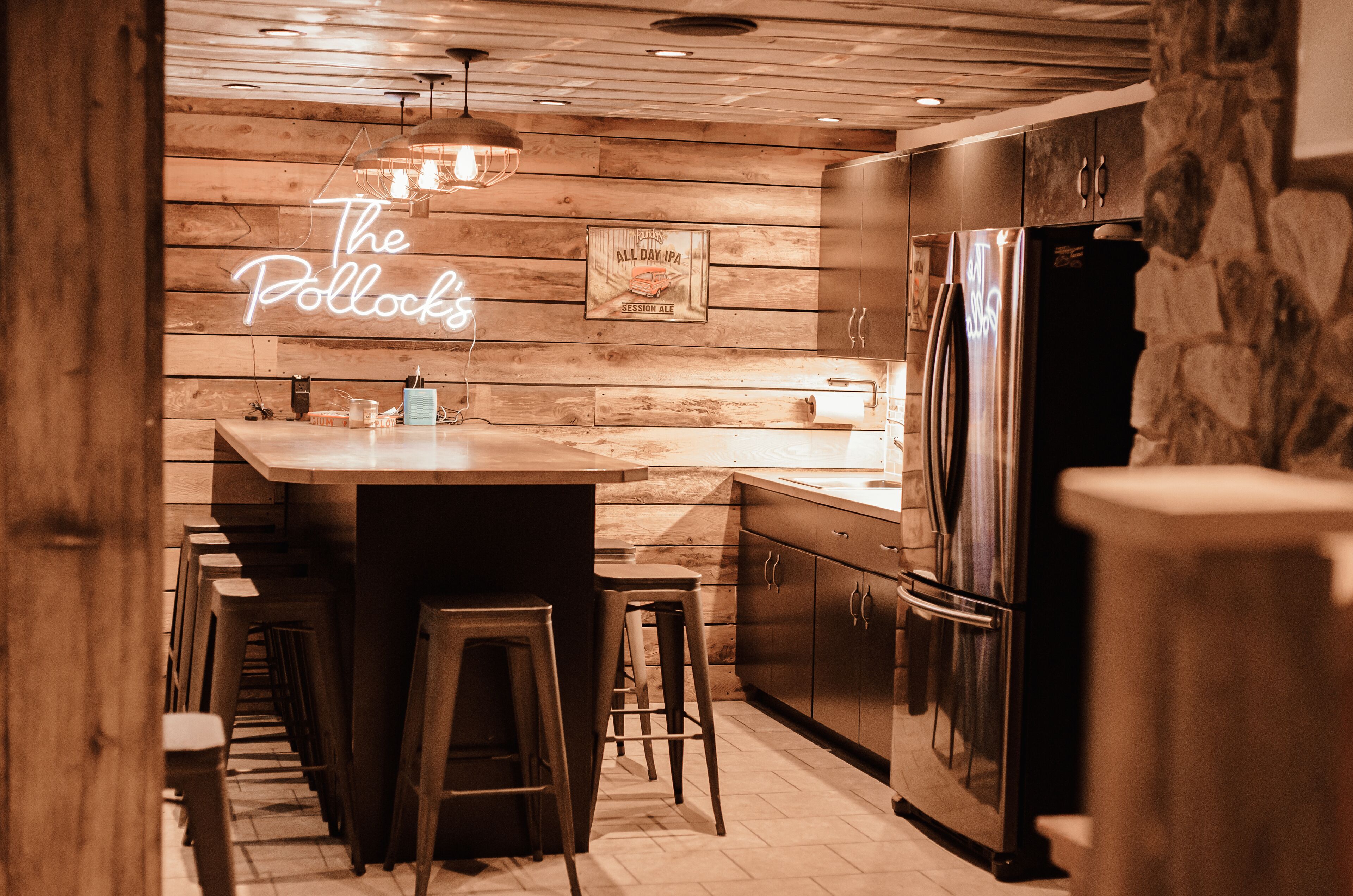 A kitchen with wooden paneling, a neon sign, stainless steel appliances, and bar stools.
