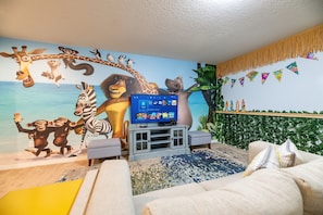 Sala de estar com um grande mural de personagens animados, uma televisão e uma planta.
