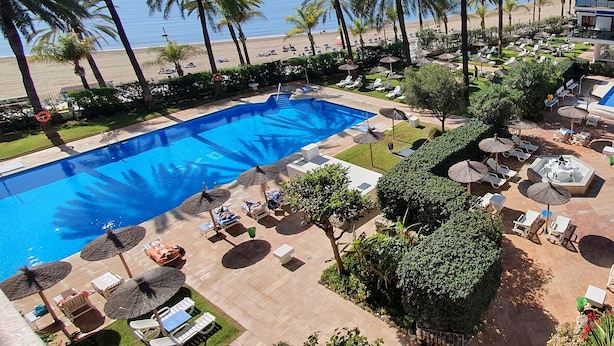 A pool area with lounge chairs and umbrellas, surrounded by palm trees and a view of the beach. - Skol 521 - Fantastic Beachfront Studio Holiday Home (Marbella)