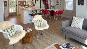 A modern living room with a grey sofa, a white armchair with a fluffy throw, and a coffee table with magazines and a phone. - Arthouse, freshly renovated 2 bedroom residential (North Charleston)