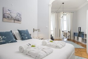 Een hotelkamer met een bed, een fietskunstwerk aan de muur, een televisie en een balkon met gordijnen.