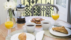 Ein Frühstückstisch mit Croissants, Kaffee und Orangensaft auf einem Balkon mit Blick auf Grünflächen.
