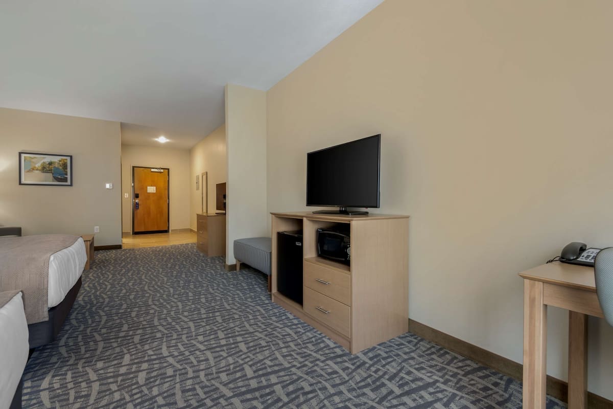 Een hotelkamer met een bed, een bureau met een computer, een televisie en een magnetron.