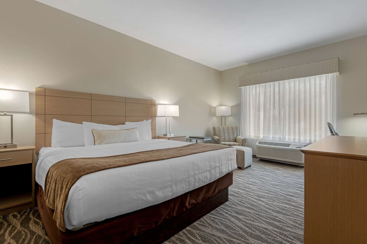 Een hotelkamer met een groot bed, nachtlampjes, een bureau en een stoel.