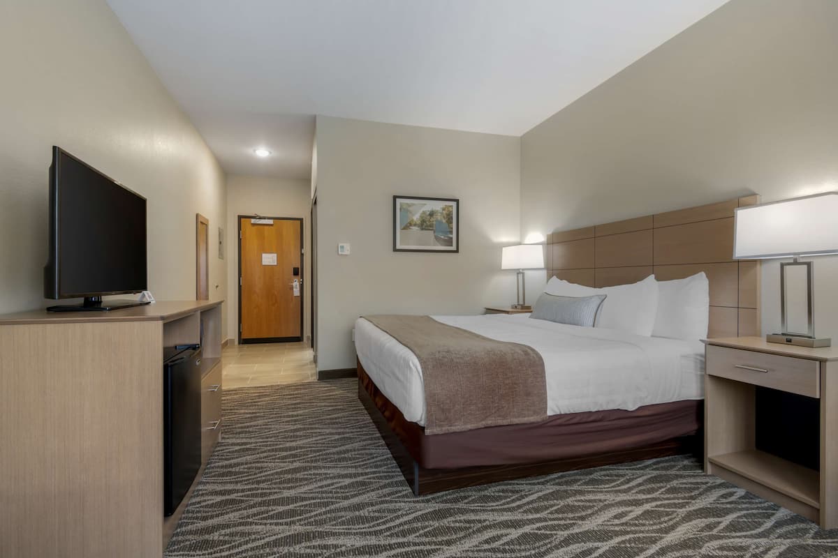 Een hotelkamer met een bed, nachtkastje, lamp, televisie en een klein bureau.