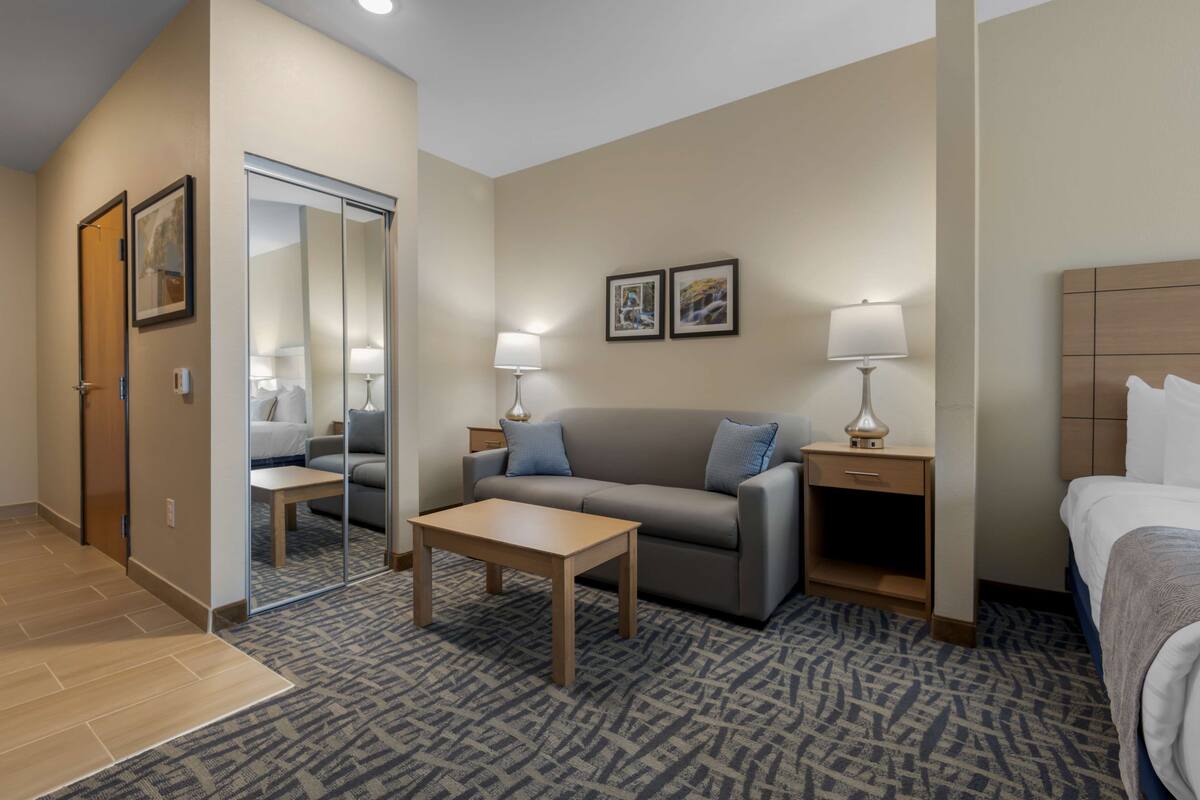 Een hotelkamer met een bank, een klein tafeltje, een bed, een nachtkastje met een lamp, een spiegel en twee ingelijste foto's aan de muur.