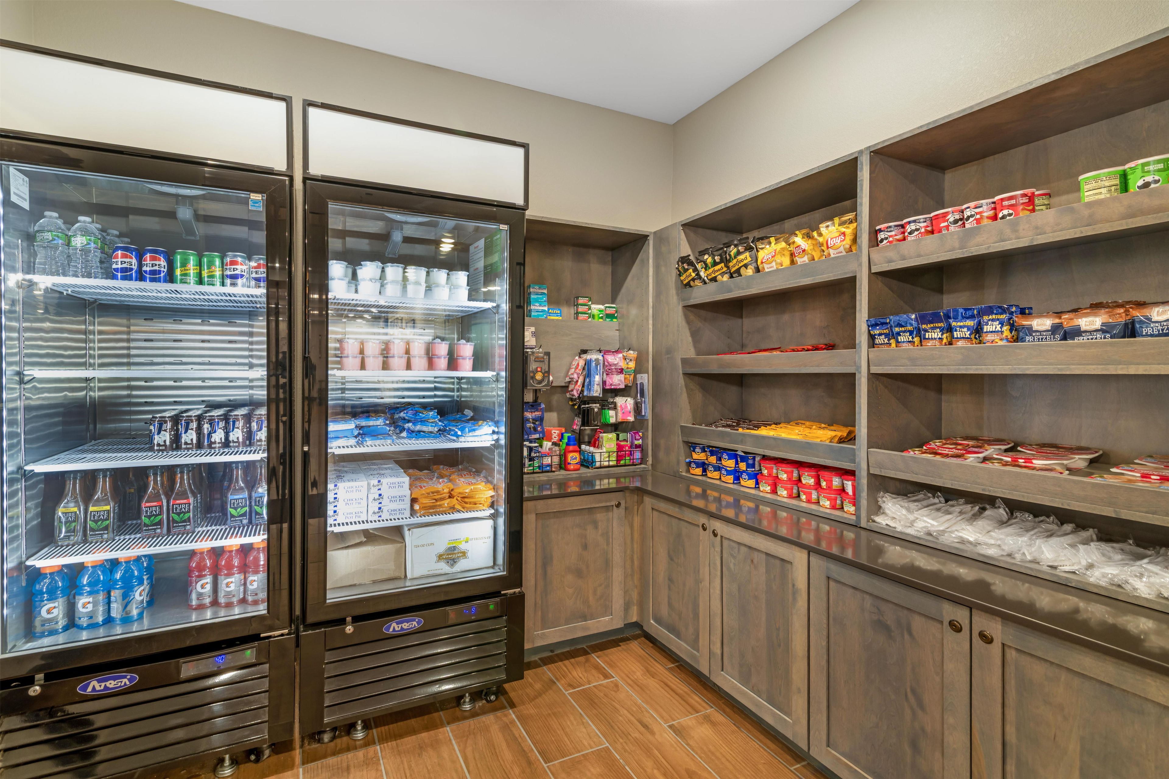 Un espace de libre-service où l’on peut se servir des boissons, avec un choix varié, ainsi qu’une étagère remplie de snacks, notamment des chips et des bretzels.