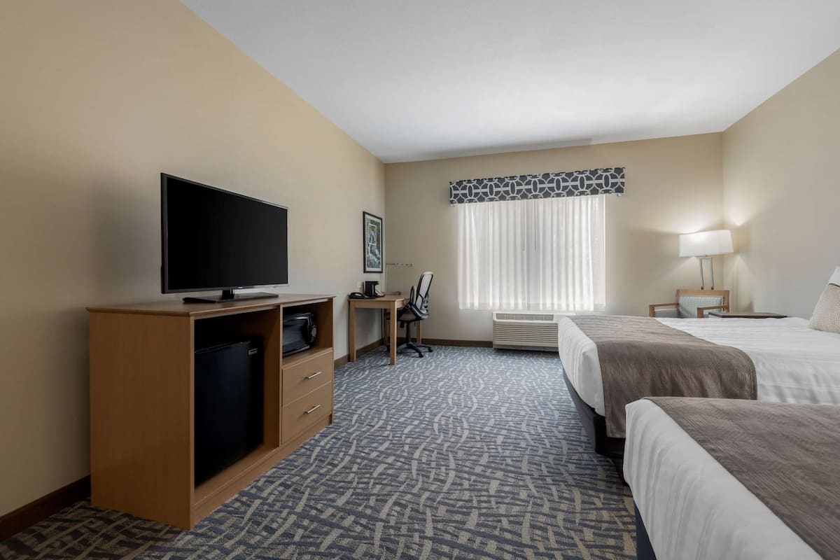 Een hotelkamer met een flatscreen televisie, een bureau, een stoel, een bed en een raam met gordijnen.