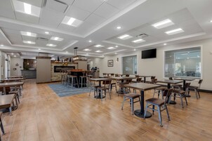 Un comedor amplio con varias mesas y sillas, una zona de cocina y un ventanal que proporciona luz natural.