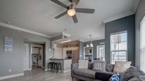 A modern living room with a gray sofa, black barstools, and a ceiling fan. - PATHWAY TO THE SEA, 3RD FLOOR PENTHOUSE! HEATED POOL AND STEPS FROM OCEAN! (Corpus Christi)