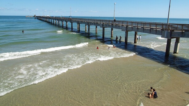 A pier extending into the ocean with people walking along it. - PATHWAY TO THE SEA, 3RD FLOOR PENTHOUSE! HEATED POOL AND STEPS FROM OCEAN! (Corpus Christi)
