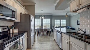 A modern kitchen with white cabinetry, stainless steel appliances, and a dining area with a view. - PATHWAY TO THE SEA, 3RD FLOOR PENTHOUSE! HEATED POOL AND STEPS FROM OCEAN! (Corpus Christi)