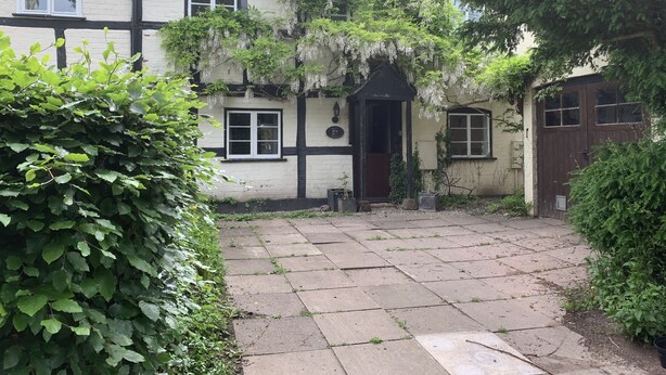 A traditional house with a tiled courtyard, a black door, and white-framed windows. - Timbered House (herefordshire)