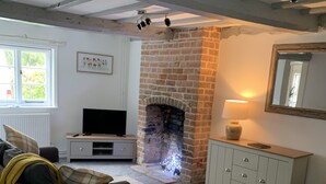 A living room with a brick fireplace, a sofa, a television, and a cabinet. - Timbered House (herefordshire)