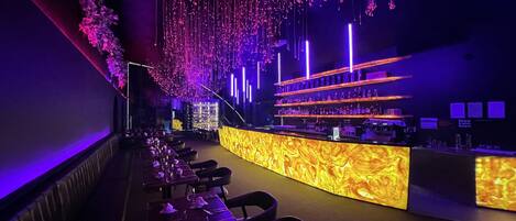 Una zona de bar con una barra alargada, diversas opciones de asientos e iluminación decorativa colgante.