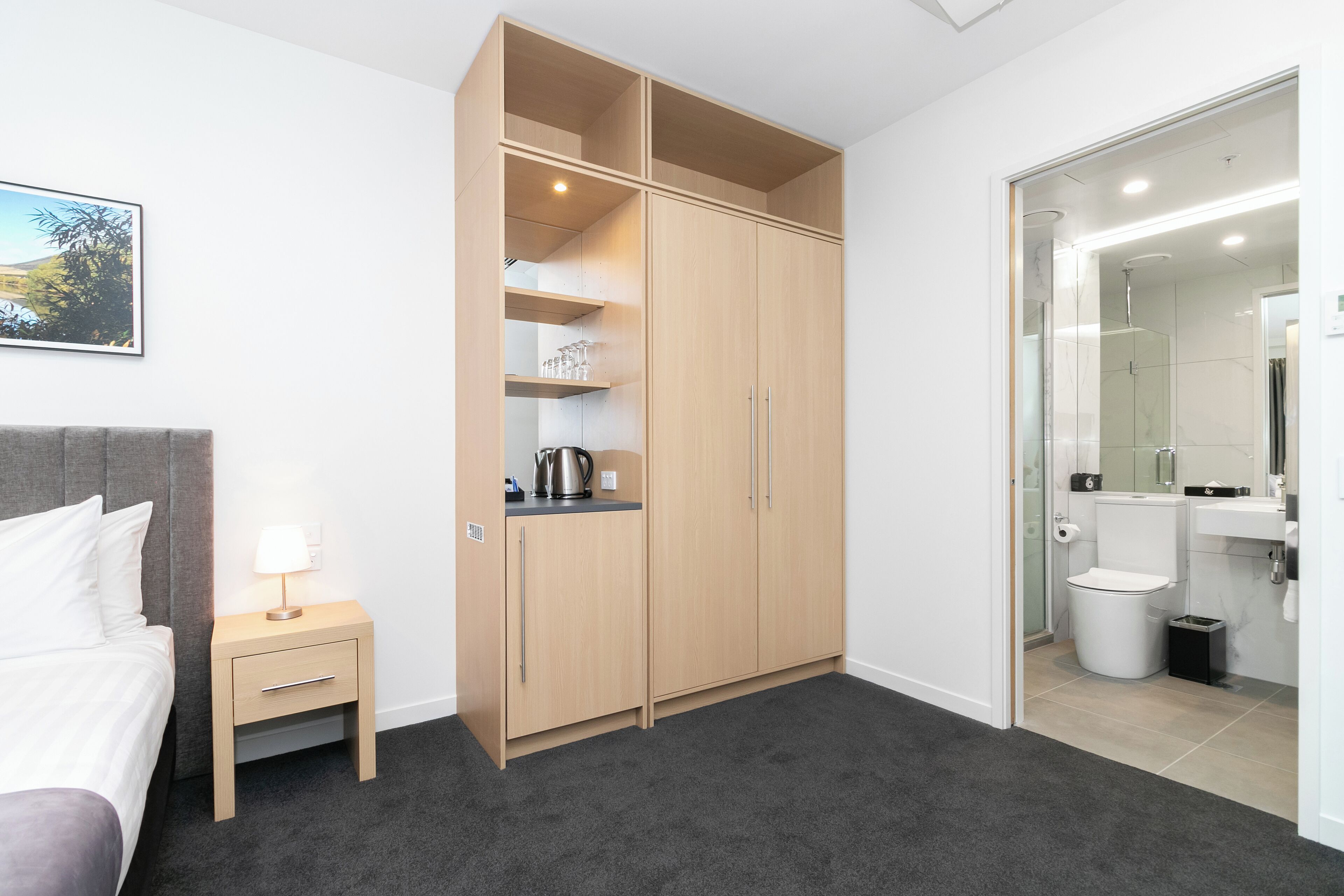 A bedroom with a bed, a nightstand, a wardrobe, and a bathroom with a shower and toilet.