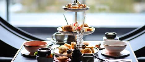 Un présentoir à étages garni de pâtisseries et un vase décoratif placés sur une table près d’une fenêtre.