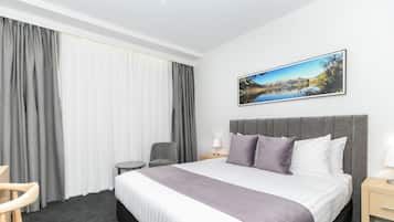 A hotel room with a large bed, a chair, a small table, and a painting on the wall.