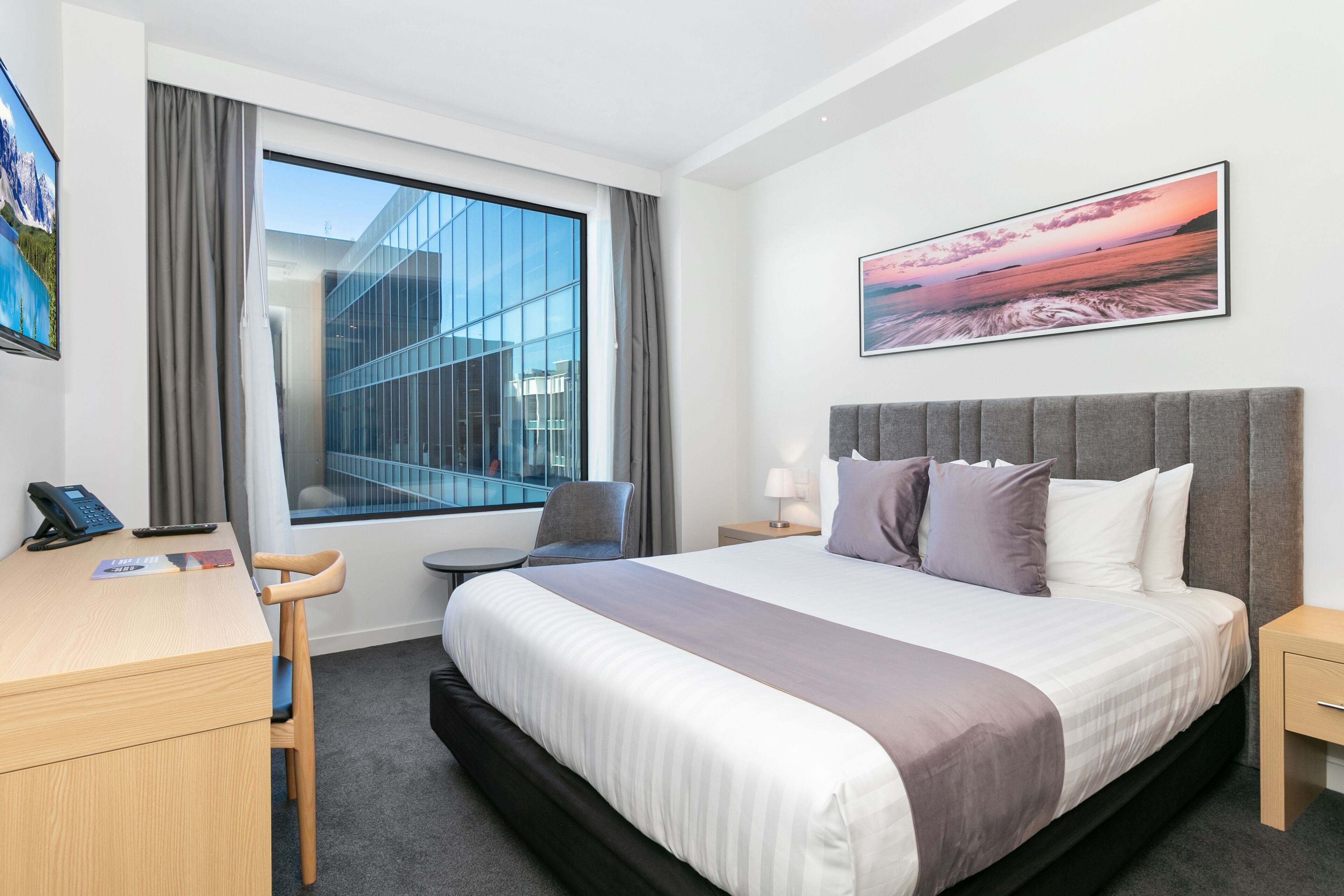Una habitación de hotel moderna con una cama grande, un escritorio con silla, una mesita y una ventana con cortinas.
