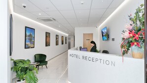 A hotel reception area with a reception desk, a green chair, potted plants, and framed pictures on the wall. - Christchurch City Hotel (Christchurch)