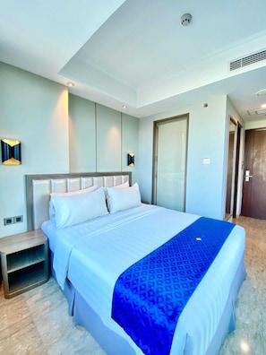 A modern hotel room with a large bed, a bedside table, a wardrobe, and a bathroom door.