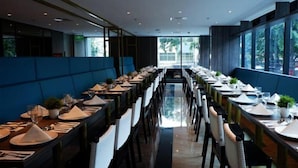 A modern restaurant with long tables and blue cushioned seating. - Arthama Hotel Tanah Abang Jakarta (Jakarta)
