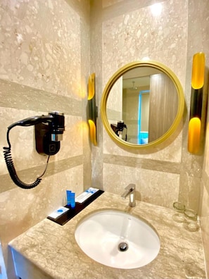 A bathroom with a marble sink, a round mirror, and a hairdryer mounted on the wall. - Arthama Hotel Tanah Abang Jakarta (Jakarta)
