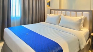 A modern hotel room with a large bed, a nightstand, and a wall-mounted light fixture. - Arthama Hotel Tanah Abang Jakarta (Jakarta)