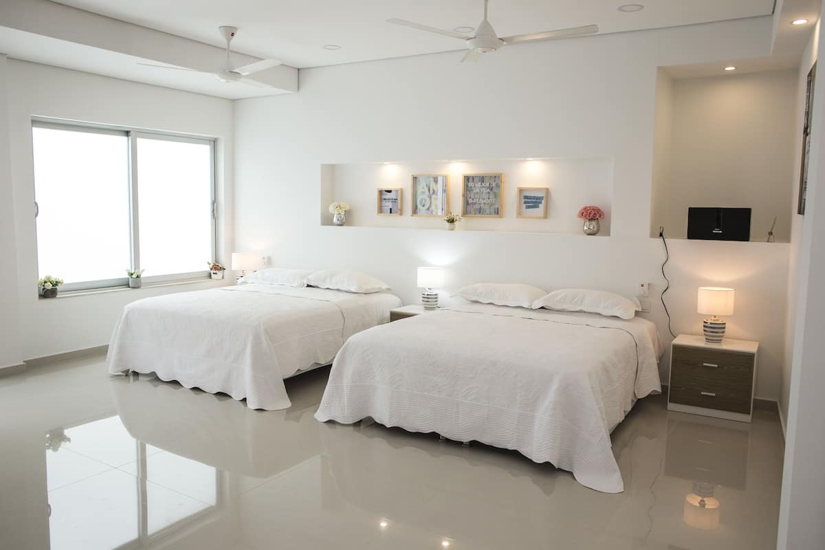 Quarto moderno com duas camas, um ventilador de teto, uma janela grande e obras de arte na parede.