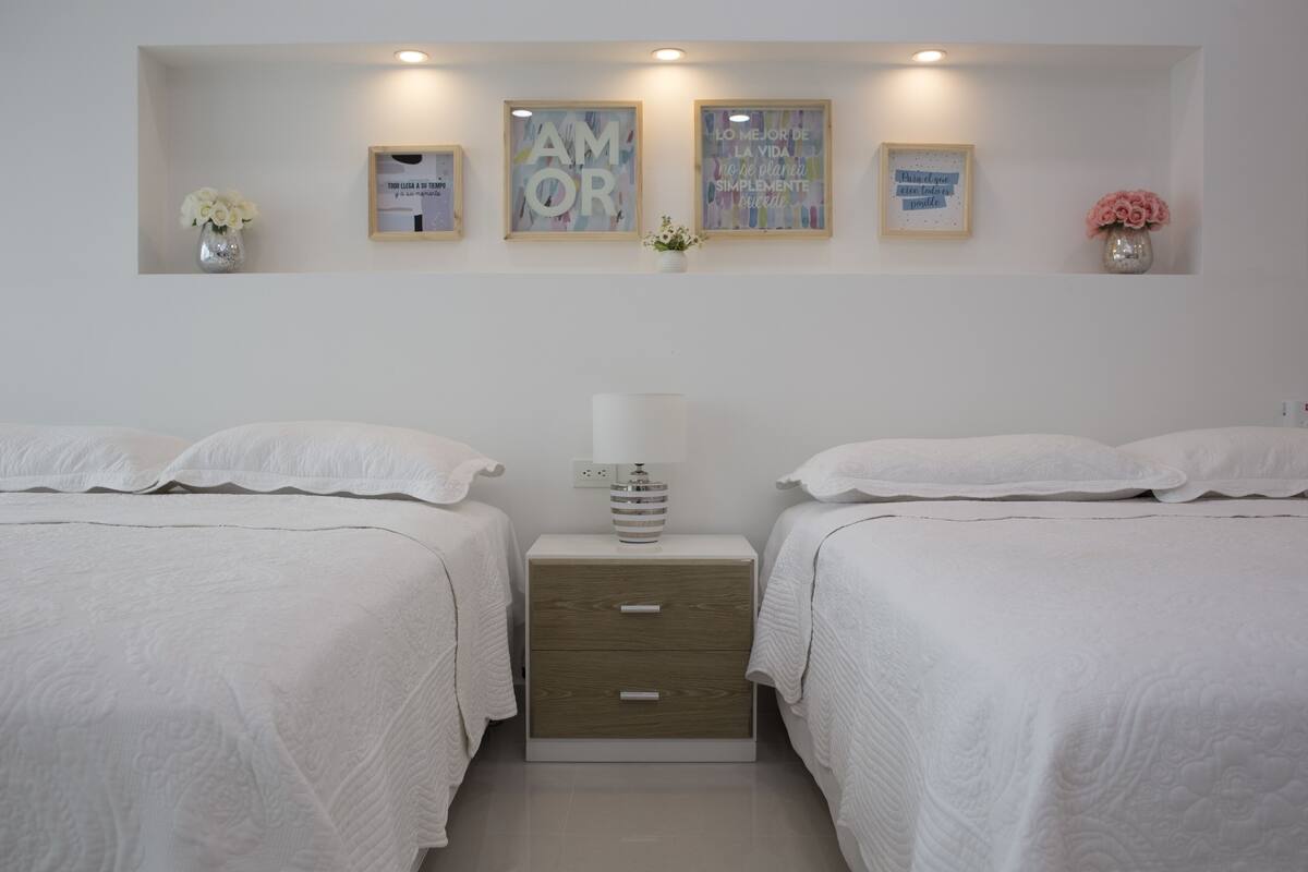 Quarto com duas camas, mesa de cabeceira com abajur e decoração na parede.