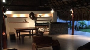 Área externa com mobiliário de madeira e estrutura de telhado de palha.