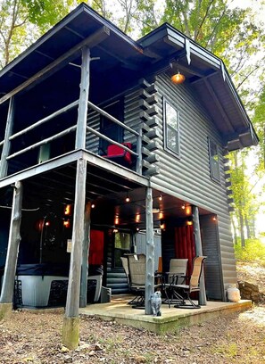 A two-story cabin with a balcony, outdoor seating, and a view of the surrounding trees. - Aunt B`s Cabin  W/  Hot Tub!  Near Table Rock Lake (Lampe)