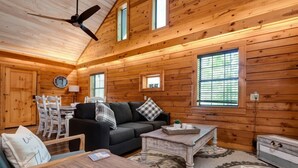 A cozy cabin interior with a wooden ceiling, a sofa, a dining table, and a coffee table. - Aunt B`s Cabin  W/  Hot Tub!  Near Table Rock Lake (Lampe)