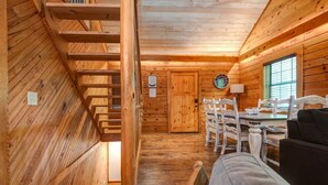 A wooden interior with a staircase, a dining area with white chairs, and a black sofa. - Aunt B`s Cabin  W/  Hot Tub!  Near Table Rock Lake (Lampe)